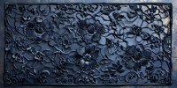 Dark floral relief pattern carved in stone or metal with dimensional flowers and leaves creating elegant textural design against dramatic shadowed background.