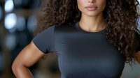Mixed race woman with natural curly hair wearing black t-shirt, confident expression against dark background. Professional headshot style portrait for business or lifestyle.