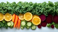 Fresh organic vegetables and fruits arranged in line on white background. Colorful healthy food composition with kale, oranges, carrots, cucumbers and beets.