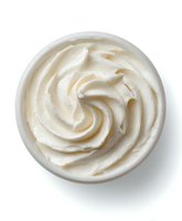 Creamy white cosmetic cream with swirled texture in round container isolated on white background for skincare and beauty product design.