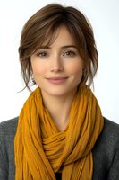 Young Caucasian woman wearing mustard yellow knit scarf and gray sweater smiling at camera with natural makeup and casual updo hairstyle against light background.