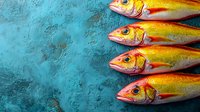 Fresh yellow and pink fish arranged in row on textured turquoise background. Raw seafood composition with vibrant colors for restaurant menu or cooking blog.