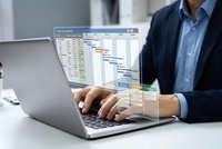 Professional businessman working on laptop with project management Gantt chart software interface for business planning and scheduling tasks.