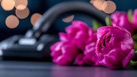 Vibrant pink tulips lying next to computer mouse on dark surface with soft bokeh lights in background, creating romantic workspace atmosphere.