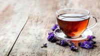 Glass cup of aromatic herbal tea with fresh purple wildflowers on rustic wooden background, natural light creates cozy atmosphere for wellness concept.