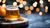 Glass jar of golden honey on wooden board with pine branch and bokeh lights creating cozy winter atmosphere. Seasonal food photography for holiday designs.