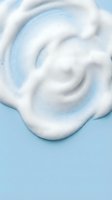 White creamy foam swirl texture on light blue background for skincare cosmetic product design and beauty advertising applications.