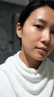 Young Asian woman with glowing dewy skin in white towel after skincare routine in modern bathroom for beauty and wellness concepts.