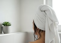 Woman with wet hair wrapped in white towel after shower in modern bathroom with plant for spa and wellness concepts.