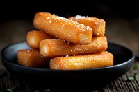 Crispy golden churros dusted with sugar served on black ceramic plate against dark rustic wooden background, close up view with selective focus and soft lighting.