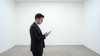Young Caucasian male professional in dark business suit standing in empty white room, holding smartphone, looking at screen. Suitable for corporate, technology, and business concepts.
