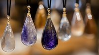 Crystal teardrop pendants in clear and purple amethyst hanging on golden hooks against warm blurred background, creating magical jewelry display.