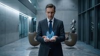 Middle-aged Caucasian businessman in dark suit holding glowing holographic projection in modern corporate office lobby with futuristic lighting and design.