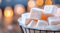 White marshmallows in metal bowl with warm bokeh lights background for cozy winter treats and hot chocolate desserts.