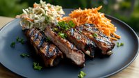 Grilled pork ribs with char marks served on dark plate, garnished with fresh herbs, accompanied by creamy coleslaw and shredded carrot salad side dishes.