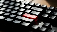 Close-up of computer keyboard with single red key highlighted among black and white keys, representing urgency, alert or special function in technology.