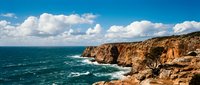 Dramatic coastal cliffs with turquoise ocean waves and white clouds, perfect for travel, nature, and landscape design projects.