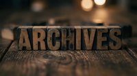 Vintage wooden letterpress blocks spelling ARCHIVES on rustic wood surface with warm bokeh lights creating atmospheric background for historical documentation concepts.