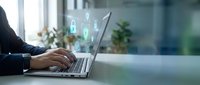 Professional businessman working on laptop with digital security icons and data protection symbols floating above screen in modern office environment.