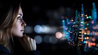 Young Caucasian businesswoman looking at futuristic holographic city projection with glowing lights and bokeh effect, concept of digital transformation and smart cities.