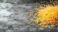 Golden yellow lentils scattered on dark textured surface with dramatic lighting creating warm glow for cooking and nutrition concepts.