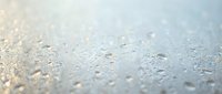 Water droplets on glass surface creating abstract bokeh pattern with soft blue and white tones for backgrounds and textures.