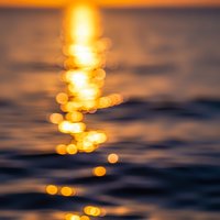 Golden sunset reflection creates dreamy bokeh lights dancing on calm ocean water surface during peaceful evening hour for relaxation and meditation concepts.