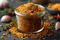 Homemade aromatic spice blend in glass jar with fresh herbs and garlic on dark background, perfect for seasoning meat, fish and vegetables in cooking.