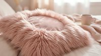 Fluffy pink pet bed with soft faux fur rim on white bedding, ideal for cat or small dog comfort and home decor styling.