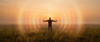 Man with arms outstretched in field at sunrise with energy waves radiating around him symbolizing freedom, meditation, spiritual awakening and personal growth.