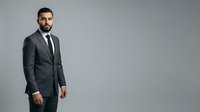 Professional man with dark beard wearing charcoal suit and black tie stands against neutral background, suitable for corporate, business, and professional website use.