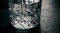 Crystal cut glass tumbler with geometric diamond pattern on dark wooden surface for luxury beverage service and elegant dining experiences.