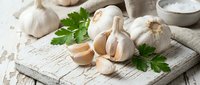 Fresh garlic bulbs and cloves with parsley on rustic wooden cutting board. Organic cooking ingredients for healthy Mediterranean cuisine and culinary preparations.