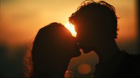 Romantic couple silhouette kissing at golden sunset, intimate moment between man and woman against warm orange sky, love and relationship concept.
