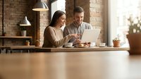 Young professional couple working together on laptop in modern office space with brick walls and natural lighting for business collaboration.