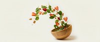 Fresh strawberry leaves and berries floating from wooden bowl on neutral background for healthy eating and organic food concepts.