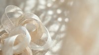 Delicate ivory ribbon bows with shimmering beads on soft blurred background, suitable for wedding invitations, gift wrapping, and festive decoration projects.