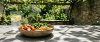Healthy grain bowl with chickpeas, roasted vegetables, and fresh greens on a rustic outdoor table in a sunny garden setting.