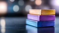 Colorful stacked erasers in gold, purple and blue on dark background with soft bokeh lights, close up view of school and office supplies for creative design.