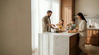 Happy family cooking together in modern kitchen with marble island counter preparing healthy breakfast meal at home.