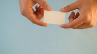 Two hands holding blank white card against light blue background for business branding and contact exchange.