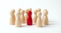 Red wooden pawn figure standing out among natural wood pawns on white background. Leadership, uniqueness and team management concept for business presentations.