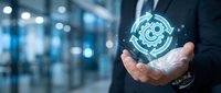 Businessman in dark suit holding glowing gear mechanism hologram in palm, symbolizing technology, innovation, and digital transformation in modern corporate environment.
