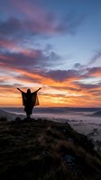Woman celebrating freedom with raised arms on mountain peak during dramatic sunrise over misty valley landscape for wellness and achievement concepts.