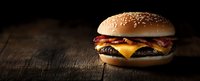 Juicy cheeseburger with melted cheese, beef patty, and fresh vegetables on sesame bun against dark wooden background in dramatic lighting. Food photography.