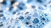 Close-up macro shot of water droplets and bubbles on surface creating abstract pattern with soft blue tones and bokeh light effects for backgrounds.