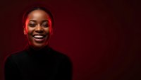 Happy young African American woman smiling with red lighting effect on dark background for portrait photography and lifestyle content.