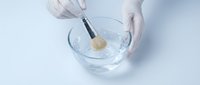Laboratory technician in white gloves using pipette to drop sample into glass bowl for scientific research and medical testing procedures.