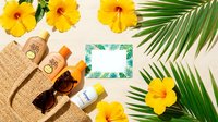 Tropical summer vacation flat lay with yellow hibiscus flowers, palm leaves, straw hat, sunglasses and sunscreen bottles on beige background for travel design.
