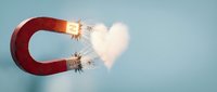 Red horseshoe magnet attracting glowing white hearts with sparks and energy effects on light blue background for love attraction concept.